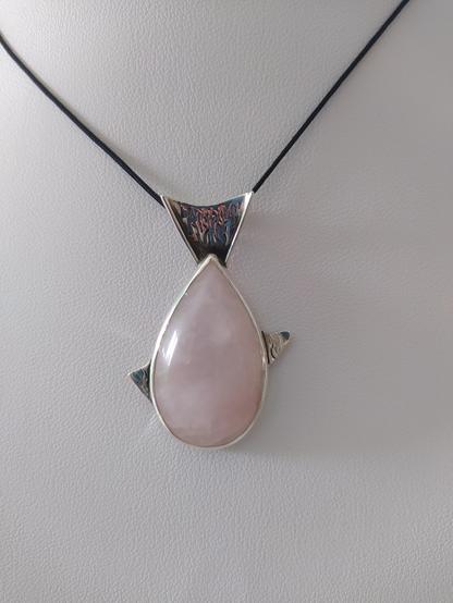 a fish shaped silver pendant with a teardop shaped pink gemstone as the main body of the fish. it has a black cord