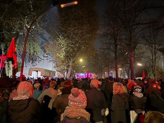 Bild von der Kundgebung, viele Menschen von hinten fotografiert die auf die Bühne blicken. Links ein Teil des Mahnmals Levetzowstraße.