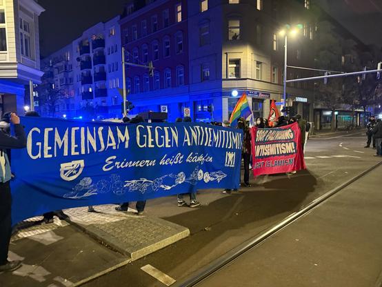 Die Demo von der Seite fotografiert, auf einem blauen Transpi steht ‚Gemeinsam gegen Antisemitismus, erinnern heißt kämpfen‘.