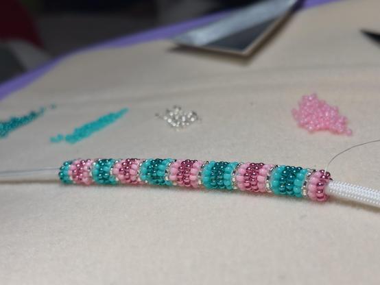A piece of pink, turquoise, and silver striped beaded paracord on a bead mat