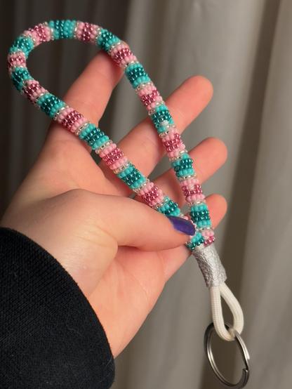 A hand holding a pink, turquoise, and silver striped beaded paracord wristlet key chain