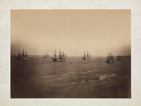 An ocean view with numerous 19th-century sailing ships in the distance. The image is divided vertically in half, with a cloudless sky at the top and the dark ocean at the bottom. The ships sit in a row along the dividing line between lightness and darkness.