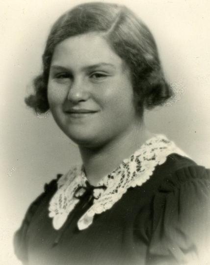 Vintage black and white portrait of a smiling woman with curly hair, wearing a dark blouse with a lace collar.