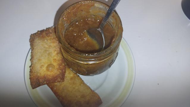 Two egg rolls on a plate with a jar of homemade plum sauce canned this summer, with a spoon in the jar