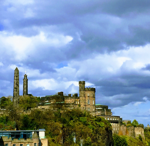 Panoramic photo of a monument and observatory. Looks like a fort on a hill. Puffy White and blueish clouds above.