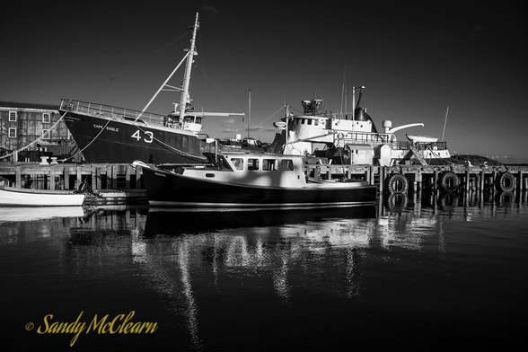 Small motor yacht and a fishing boat alongside a wharf on a calm day.