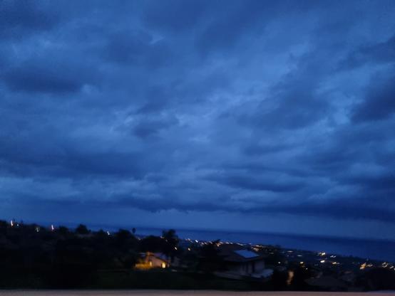 Città vista dall'alto con le luci accese di sera, mare blu intenso e cielo blu carico di pioggia