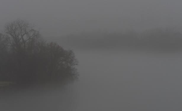 In image #1, dense fog covering the James River at Rocketts Landing in Richmond VA USA. In the left foreground is one bank of the river lightly shrouded by fog. In the background is the other bank of the river barely visible through the fog. Processed in ON1 Photo RAW 2023.