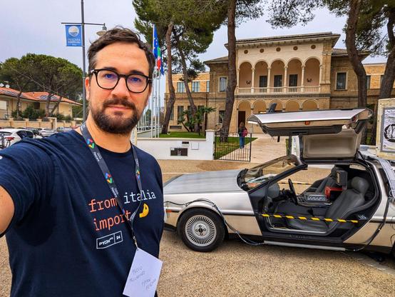 Paolo taking a selfie with a replica of the DeLorean time machine from the movie Back to the Future, and in the background, the ex-Aurum building in Pescara