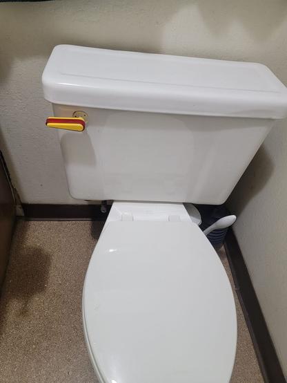 A standard white porcelain toilet with the lid closed

Where the 'flush' handle should be there is a yellow pinball flipper wrapped in a red bumper with the trademark Williams 'W'

Taken at Pinball Pirate in Benecia, CA