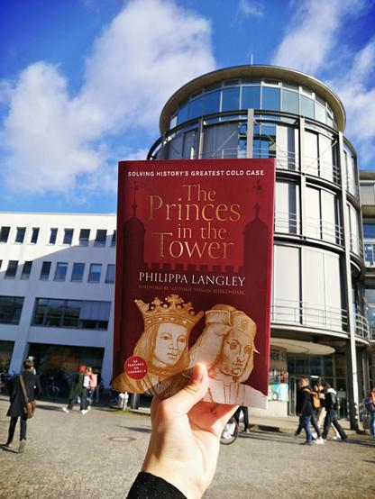 Holding the book "The Princes in the Tower" in front of the little cafeteria tower of SUB Göttingen