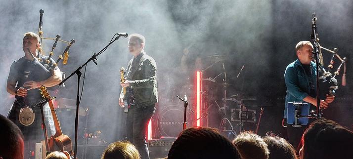 Photo of three musicians from the band Skerryvore performing on stage. Left and right bagpipes, in the middle guitar. The musicians facing the audience.