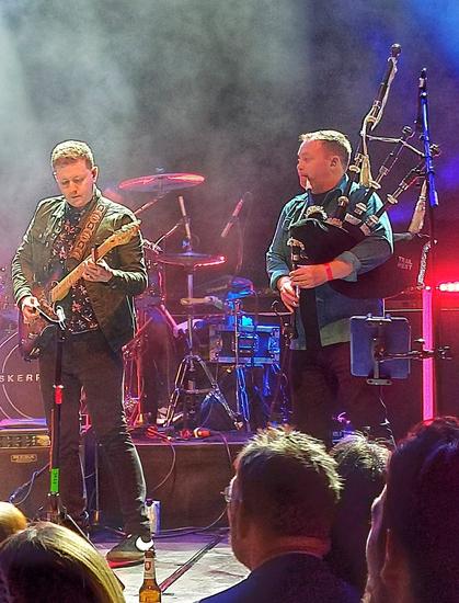 Photo of two musicians from the band Skerryvore. Left guitar, right bagpipes. In the background you see the drum set.