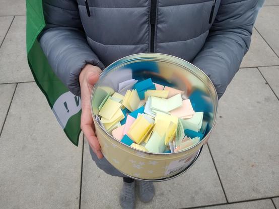 Ein Topf gehalten von einem Mensch mot vielen Zetteln drinnen.