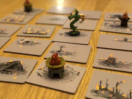 The same game boarded in the first photo, except all of the tiles are now gray, and the plant life depicted on them aflame. The human miniatures are gone. The cottage miniatures now feature flaming roofs.

In the center of the carnage stands…

Trogdor the Burninator