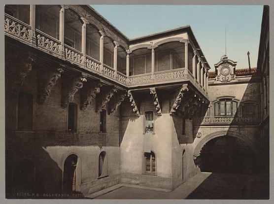 The image depicts an architectural courtyard with a historical design, likely from the late 19th or early 20th century. The structure features multiple levels of galleries supported by ornate columns and arches that create a series of enclosed spaces within the open-air environment. A prominent clock is visible on one corner building above arched windows, suggesting this may be an institutional or public space such as part of a university campus.

The courtyard appears to be devoid of people, emphasizing its architectural details rather than social activity. The monochromatic tone suggests it could either be a historical photograph in black and white or digitally altered for artistic effect. Notable features include the decorative balustrades along the galleries, the symmetry between the buildings on either side, and the play of light and shadow that adds depth to the scene.

The reference "Salamanca" indicates this courtyard is part of Salamanca's architectural heritage, possibly located in a building known as Casa de la Salina. The image captures both historical significance through its depiction of European architecture from an earlier period and serves as a reminder of patios' traditional function within urban design for leisure or public gatherings.

For visual description purposes only: no personal information about individuals should be inferred based on this still photograph, especially since it is focused solely [...]