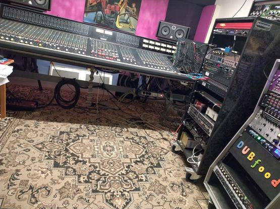 A large analog mixing console. Racks with equipment can be seen. Looks nice and homely