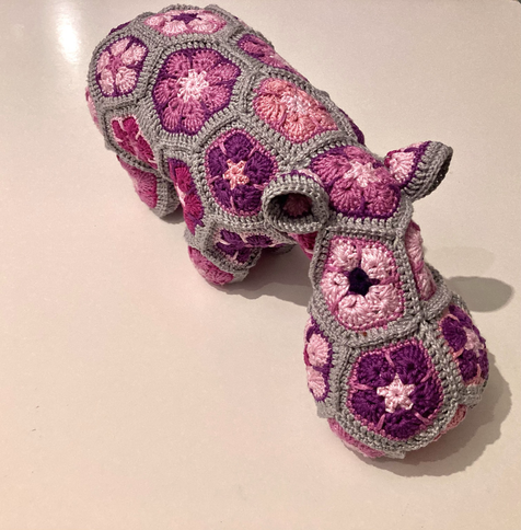 A crocheted, stuffed hippo approximately 30cms long in a pink and grey colour palette. Using the African Flower motif in the construction of the whole thing.
