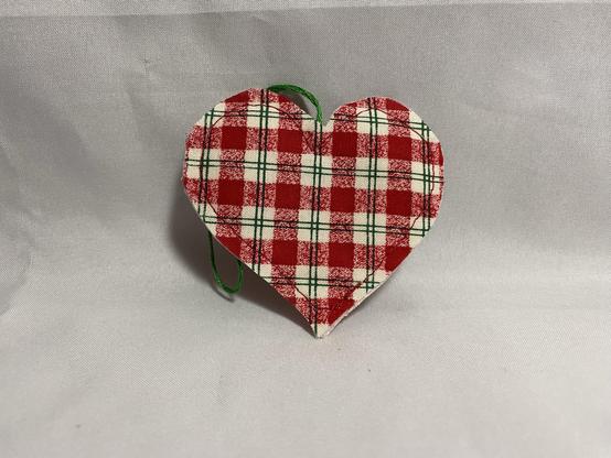 A red and white checkered fabric heart ornament with a green hanging loop, set against a light background.