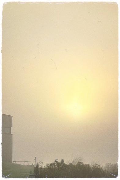 Sunrise through the mist over a lake. A building is visible to the left.