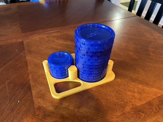 A plastic tray has two differently sized circular indents for storage lids.  Several lids are stacked on each indent.  Pillars trap the lids so they won't fall over, but the stacks are taller than the pillars.  There is an irregularly shaped hole in the corner for a handle.