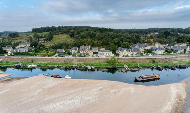 Le village du Thoureil, dans le département du Maine-et-Loire, pris depuis un drone. un banc de sable occupe le premier plan, en bas de l'image. De nombreux bateaux sont amarrés le long du quai que surplombent des maisons cossues en tuffeau et ardoise. Derrière le village, on aperçoit quelques parcelles agricoles et des massifs forestiers.