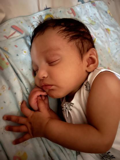 Sleeping baby with one hand on their chin and one hand in front of them.