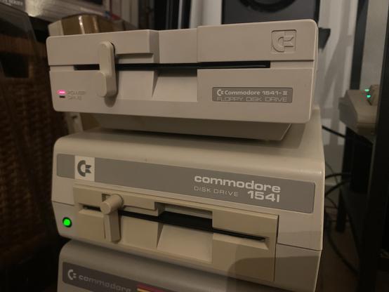 A beige 1541-II disk drive on top of a beige 1541 disk drive on top of a grey ALPS 1541.