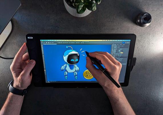 A person using a stylus to draw PlayStation's mascot Astro Bot on a digital tablet, surrounded by an organized workspace with a plant, mouse and laptop.