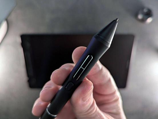 A hand holding a stylus pen above a blurred tablet screen.
