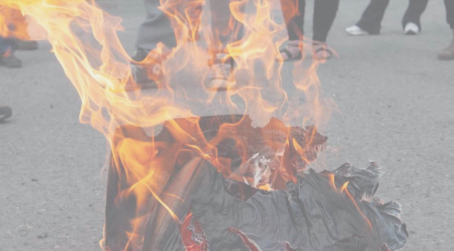 Cardboard on fire in the street, feet in the background.