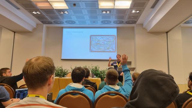 Michele Caci presenting a slide with a picture of the Ticket to Ride boardgame at GoLab 2024