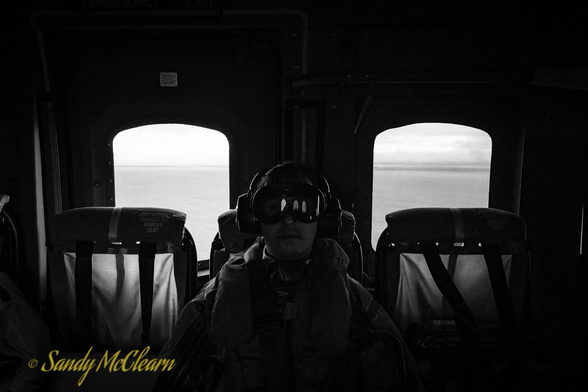 Passenger in goggles sits between two windows in a helicopter.