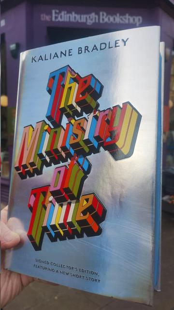 very shiny, silver cover with colourful writing for a collector's edition of Kaliane Bradley's The Ministry of Time, outside the Edinburgh Bookshop