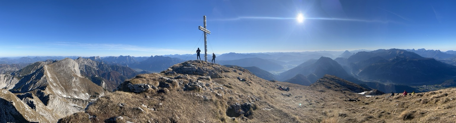 Bergpanorama mit Gipfelkreuz , 2 Personen daneben und sonnig blauem Himmel
