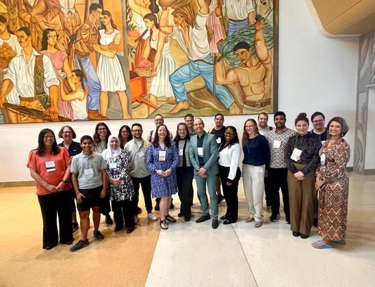 20 people stand together in front of a large mural at the San Jose (Costa Rica) convention center.