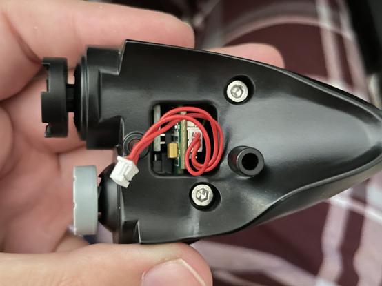 Interior side of Winwing “Shaker” module, showing a small square window with a red cable sticking out. This plugs into the top left of the joystick.