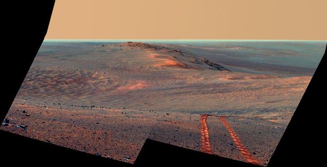 Mosaïque d'images prises par la caméra Pancam du rover Opportunity le 15 août 2014, présentées ici en fausses couleurs. Au premier plan, apparaissent des traces de roues laissées par le rover. À l'arrière plan, on voit une portion du rempart du cratère Endeavour et, à droite, l'intérieur du cratère.