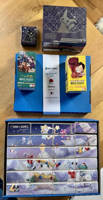 Ein Pokemon-Adventskalender, zwei japanische OnePiece Booster Packs, ein Paldean Fates ETB und ein Paket Kartenhüllen, die mit Mimikyu bedruckt sind.