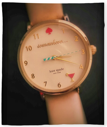 A Kate Spade lady's wrist watch with a pink band is set against a black background.  The face of the watch has a red spade at 12 o'clock with the word somewhere below that hour. There's a pink martini at 5 o'clock.  Written above the 6 o'clock hour is her name and New York.  Photography by Debra Martz  Image printed on a blanket.