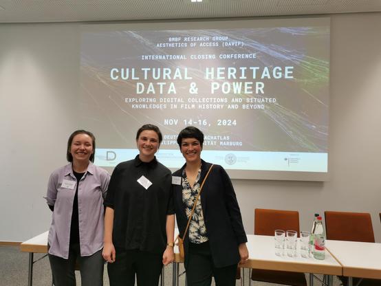 Pauline Junginger, Anne Hart & Sarah-Mai Dang standing in a room in front of slides showing the poster of the DAVIF closing conference.