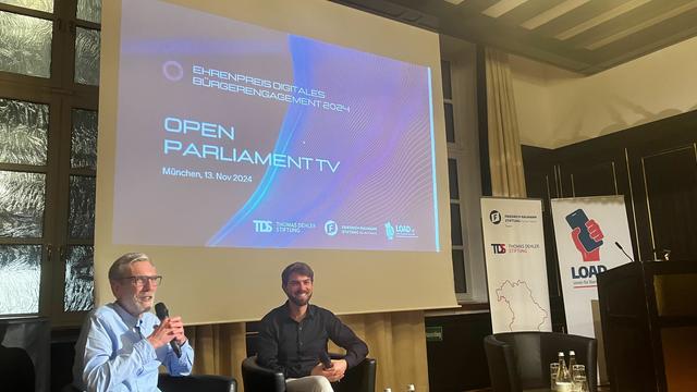 Foto der anschließenden Fragerunde, mit Präsentation "Open Parliament TV" im Hintergrund