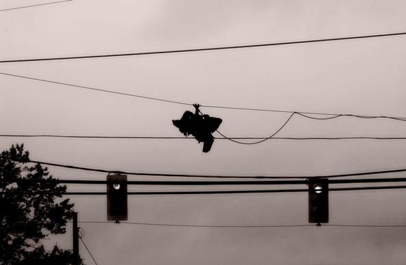 A silhouette of tied running shoes hanging from wires at an intersection