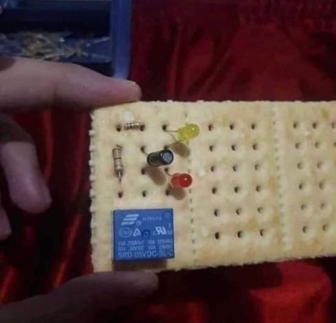 Photo of someone holding up a cracker with electronic components on it, like it's a breadboard.