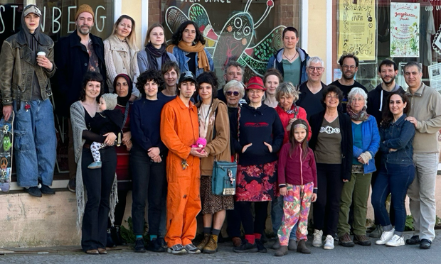 Gruppenfoto bunt gemischter Menschen - unsere Ehrenamtlichen -  vor dem Kreativraum-Projekt des Verstehbahnhofs/ Havellab eV. Im Hintergrund bemalte Scheiben mit Riesen-Schmetterling