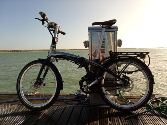 A folding bike, leaning against a shorepower outlet on a pontoon, the sea in the background.