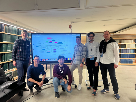 FIZ ISE team at PMDcore Hackathon II in BErlin. 5 participants in front of a huge screen with library shelfs around. Among the 5 persons, there is Dr. Joerg Waitelonis, Ebrahim Norouzi, Dr. Hossein Beygi, and Dr. Kostya Hubaev from FIZ Information Service engineering research group.