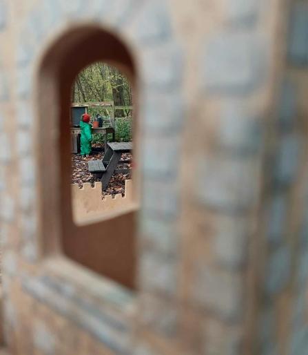 Viewing a toddler at the mud kitchen through the window of a wooden play castle.