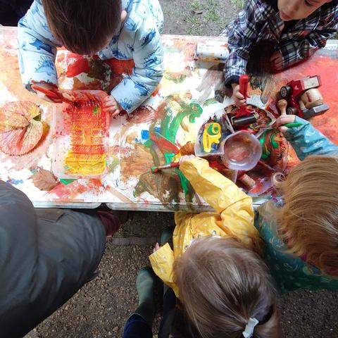 A group of toddlers photographed from above. They are using paint and other materials to make marks in autumnal colours.