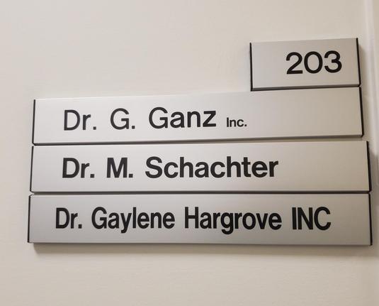A wall-mounted directory sign displays the names of three doctors: Dr. G. Ganz Inc., Dr. M. Schachter, and Dr. Gaylene Hargrove Inc. The sign is located outside office room 203.